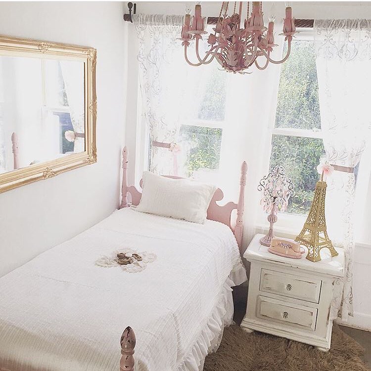 Girls bedroom with large gold mirror on wall and pink flower chandelier with white sheets and pink twin bed frame