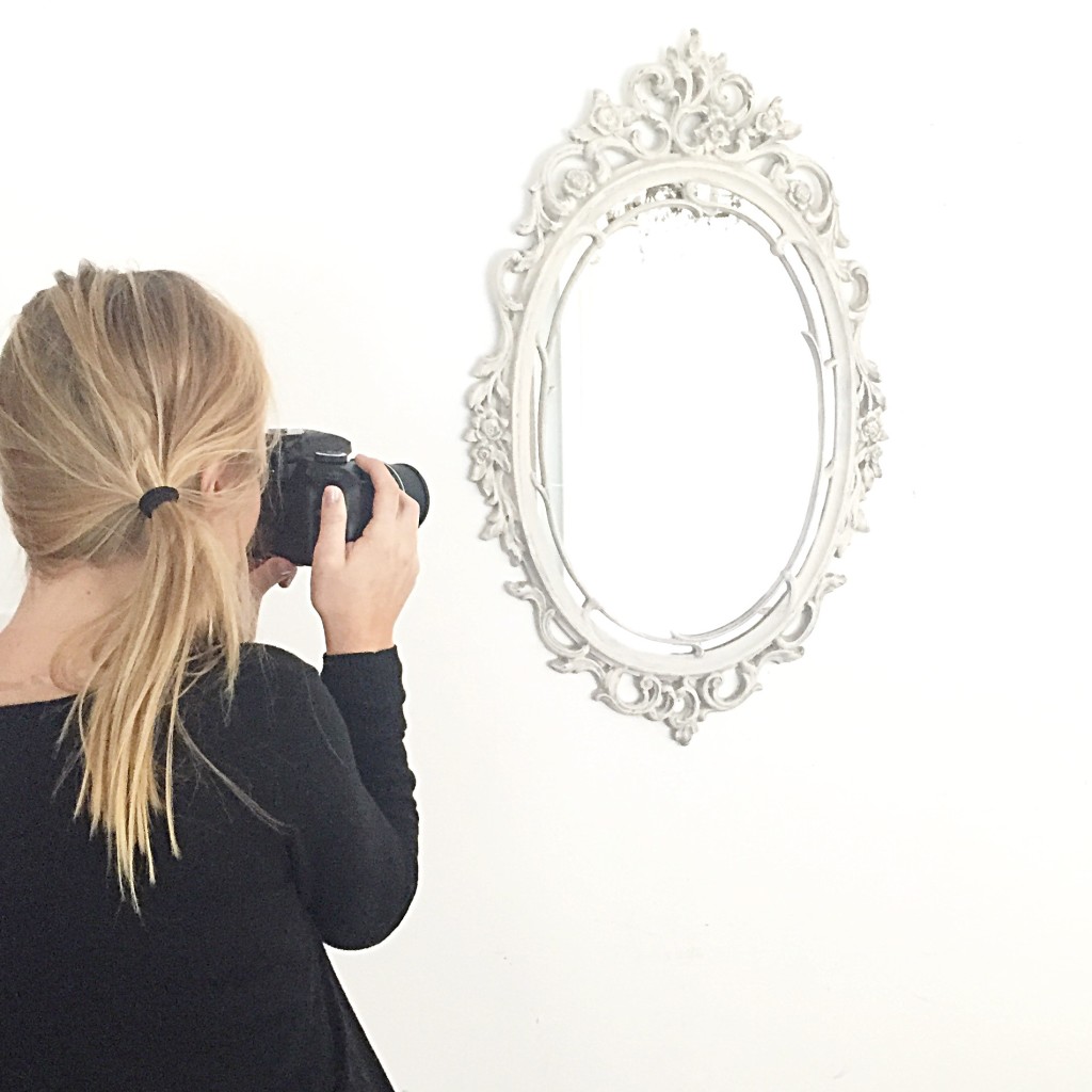 Blonde haired girl holding camera taking a picture of ornate white mirror