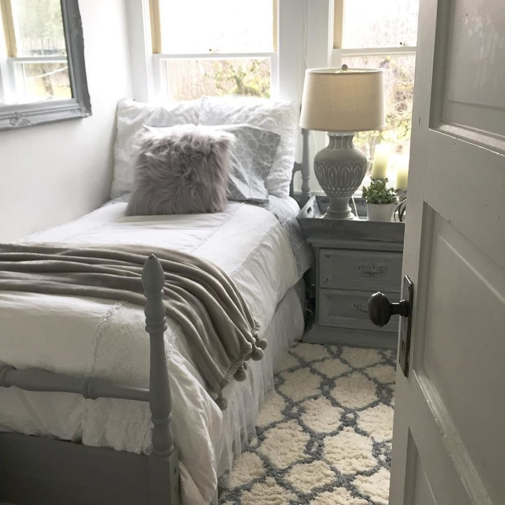 Opening to room with grey door and large grey mirror with twin bed with grey bed frame and grey fur pillow