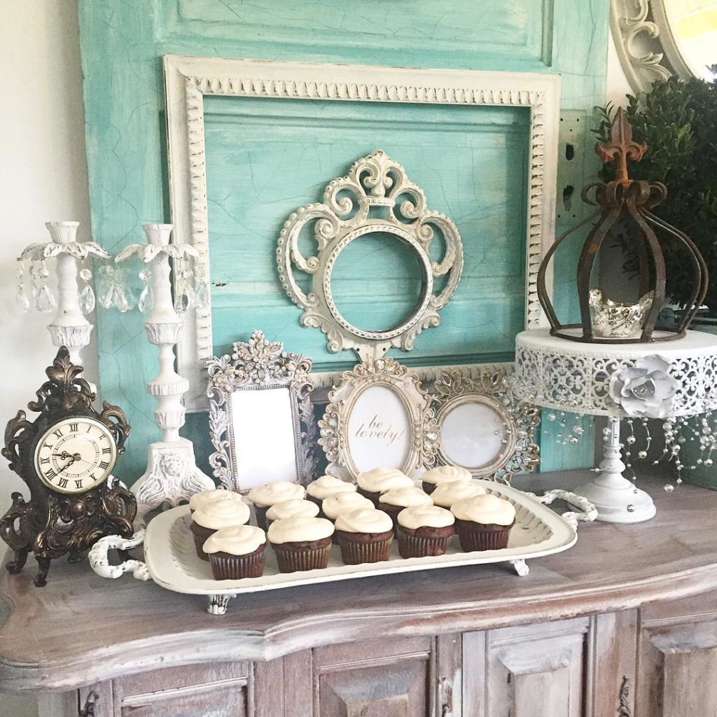 Vintage Girls Birthday Party Theme blue door with 5 white frames leaning and 2 white candle holders. white tall cake stand with rust crown and a white platter full of cupcakes