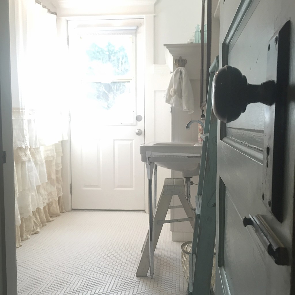 close up of doorknob leading into white floor bathroom and white cream shower curtain