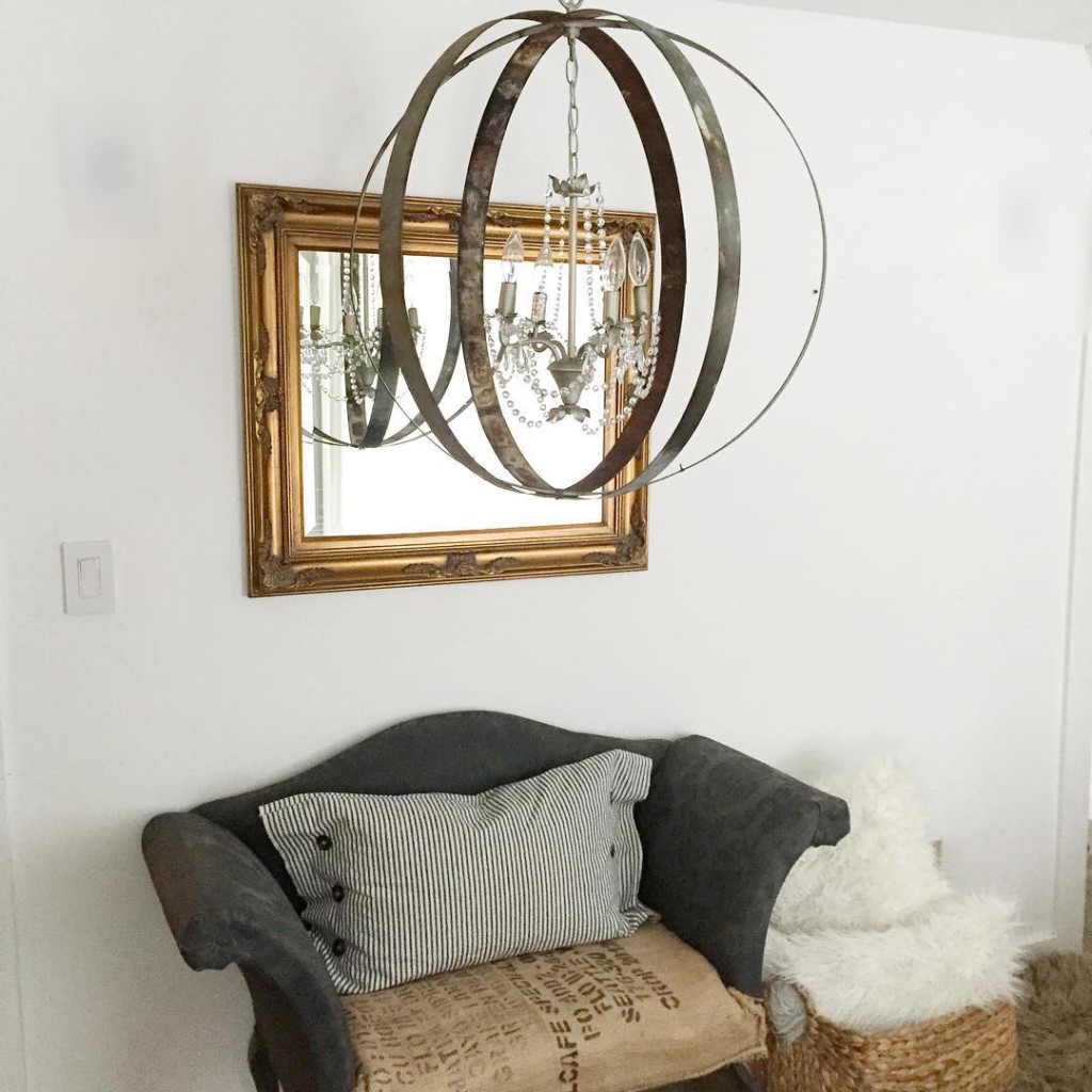 metal orb chandelier light with gold mirror behind and small gray couch with ticking stripe pillow