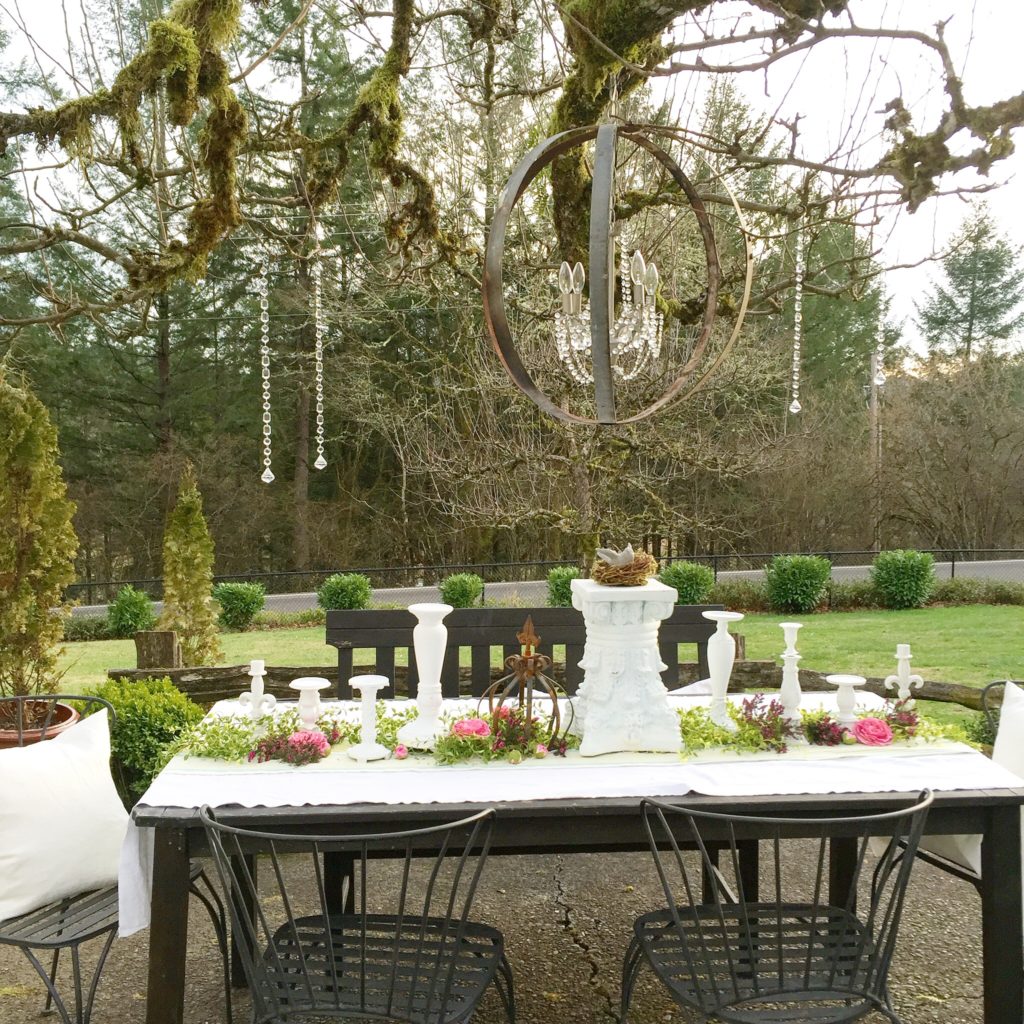 outdoot table with white tale cloth and many white candle holders with metal orb chandelier