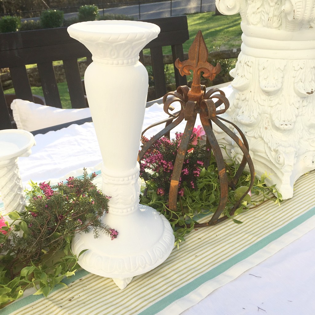 white candle holder with rust crown on top of greenery