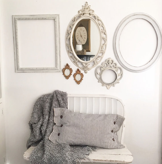 gallery wall with 3 white frames one white mirror and 2 mini gold frames with white bench below and ticking stripe pillow