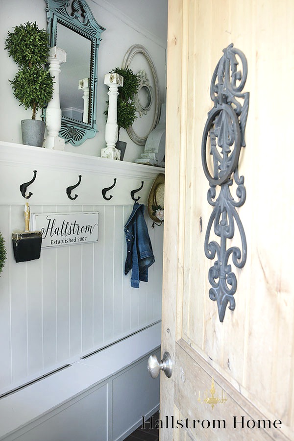 How to Decorate a Small Entryway door opeing into white mudroom with blue mirror and 2 white candle holders with black hooks