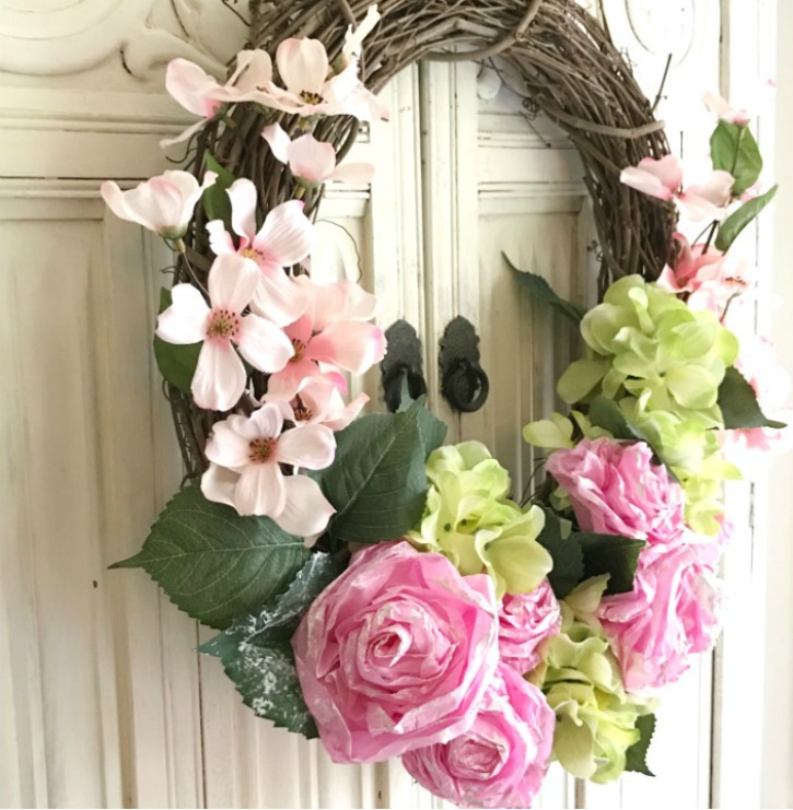 grapevine wreath with pink and green flowers against a white wall