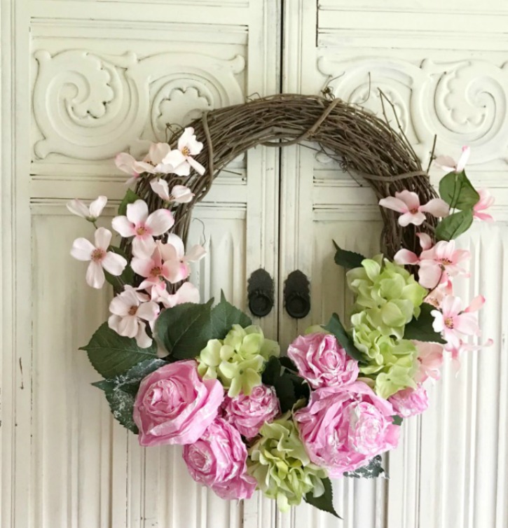 DIY Tissue Paper Flower Wreath grapevine wreath with pink and green flowers with green leaves. haning against white wall