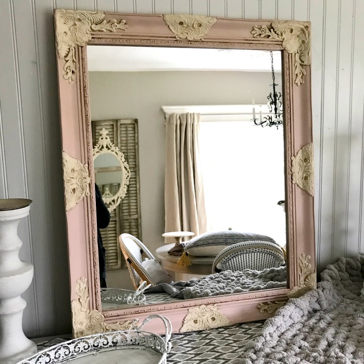 Pink and cream mirror with white candle holders by it and thick knit gray blanket