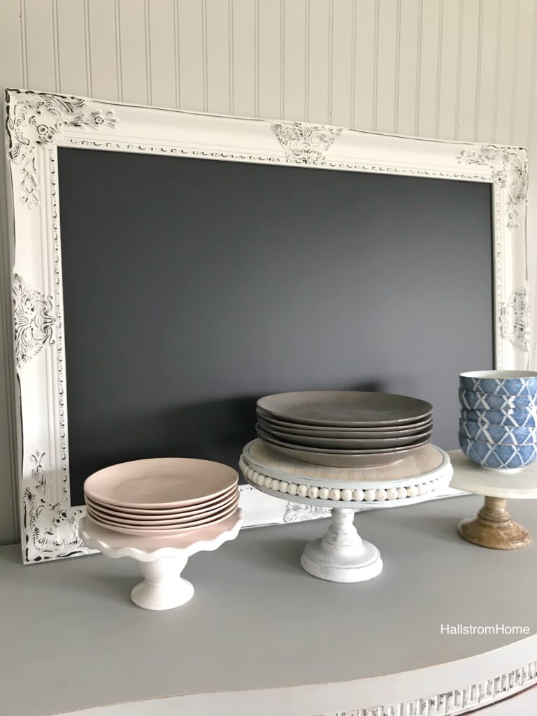 Easter Table Setting with Mini Cheesecakes white chalkboard with 3 trays in front. White tray with 5 pink plates, white tray with 5 gray plates, white tray white 5 blue bowls