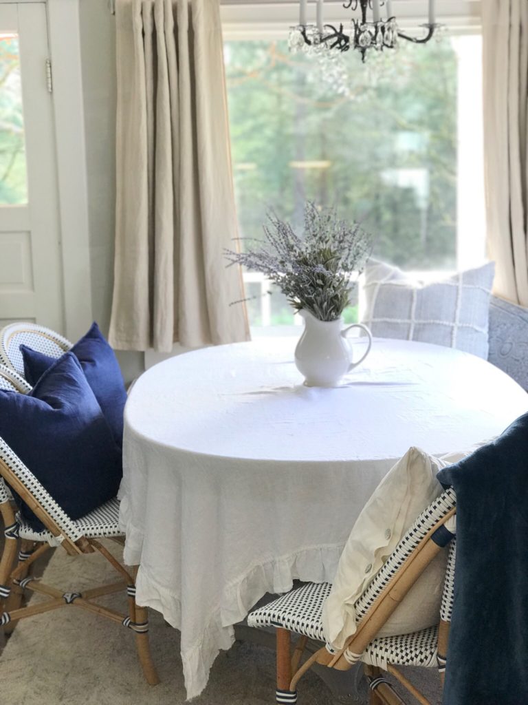 white ruffle linen table cloth with white pitcher filled white lavender and 3 chairs with 2 navy blue pillows