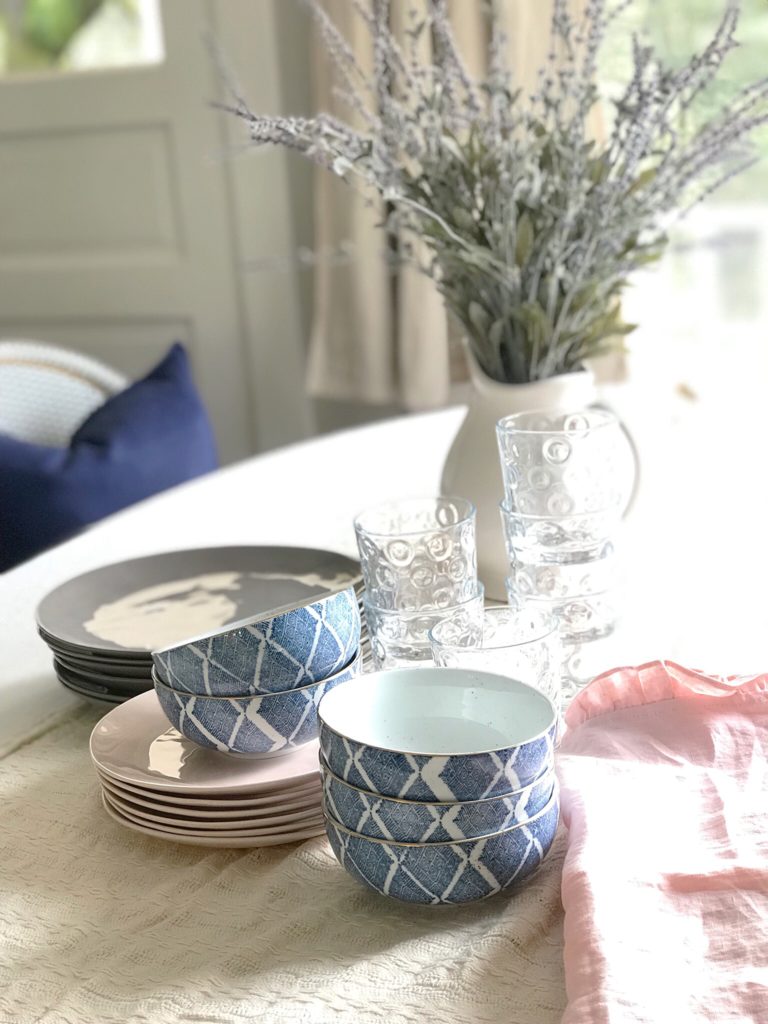 white linen table cloth with 6 clear stacked cups 5 pink stacked pltes 5 stacked gray plates, 2 blue bowls on plate and 3 bowls on side