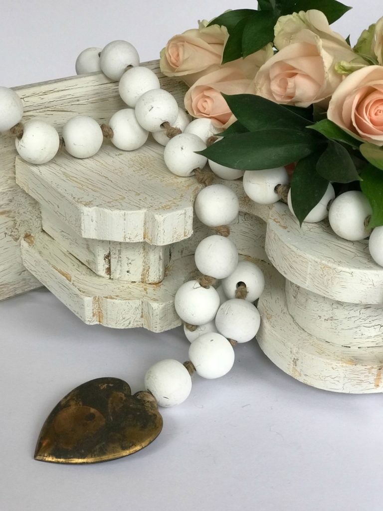 How to Make White Wood Bead Garland a white chippy corbel with white wood bead garland draped ontop. bead garland has metal heart at the end and pink roses set ontop of corbel