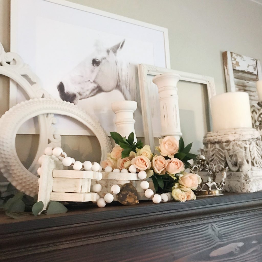 mantel with white corbel and pink roses with white bead garland and 3 white frames and 2 white candles holder, white horse picture hanging