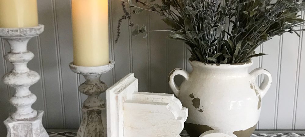 How to Chippy Paint Corbels white corbel on its side with 2 white distressed candle holders with cream candles and white pot with lavendar