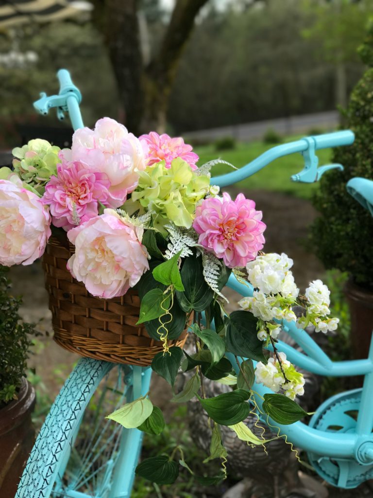 Easter Table Setting with Mini Cheesecakes blue painted bike with wicker basket on fronr. filled with pink and green flowers