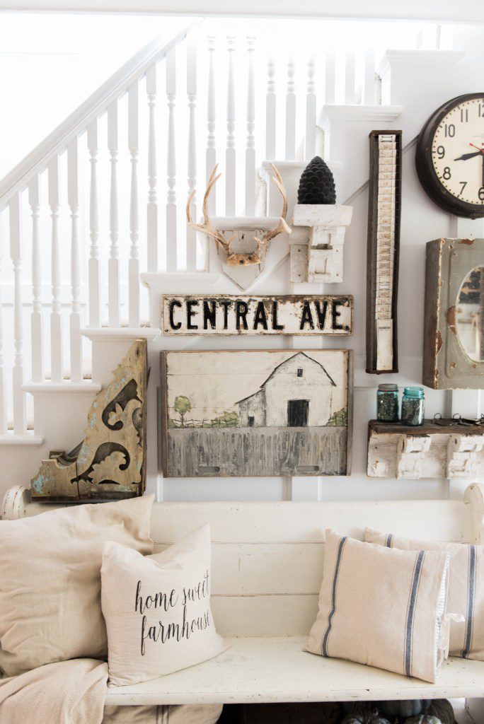 gallery wall by stairs. corbel barn painting antlers, white bench with 4 pillows