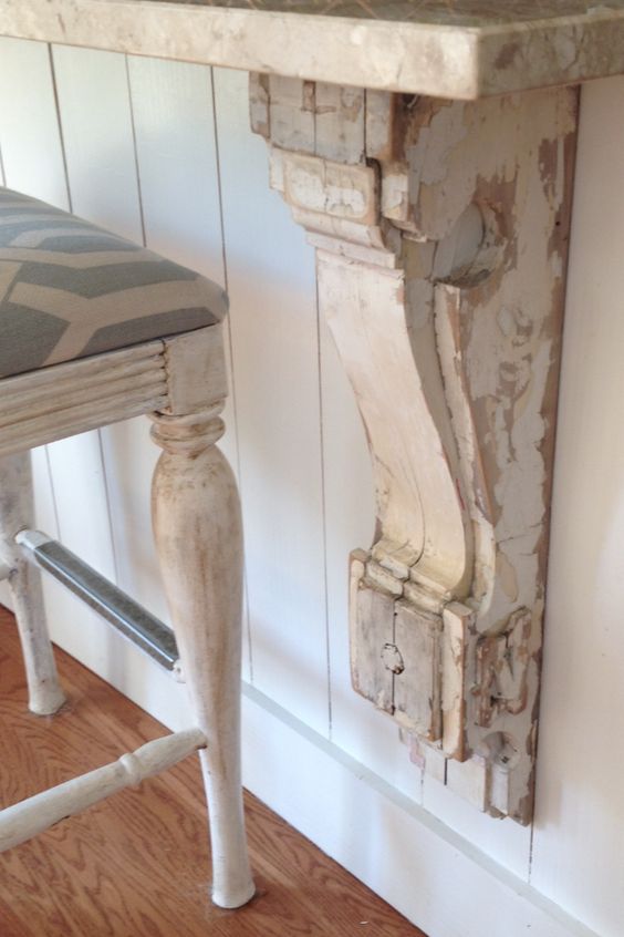 white chippy painted corbel under a marble counter with a bar chair thats white washed and has blue and white cushion