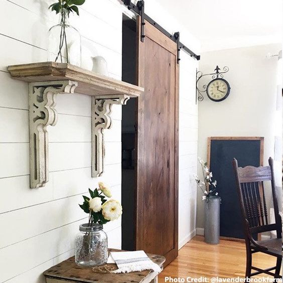 white corbels used as shelf. sliding barn door and under shelf little table with 3 white flowers in a large mason jar