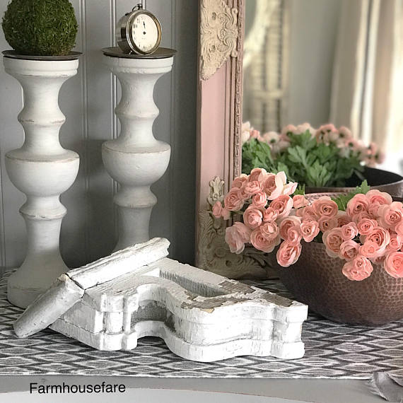 chippy white corbel with 2 candle holders and a copper bowl with pink flowers and a pink and white mirror behind that