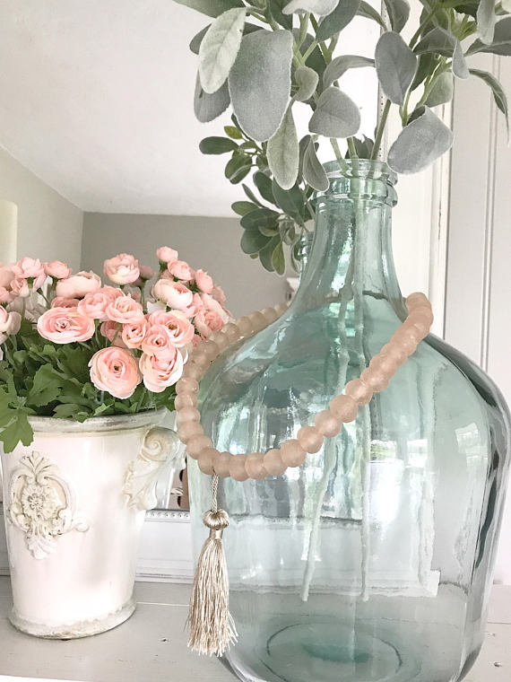 large glass jar with pink glass beads draped around. white vase with pink flowers to the left