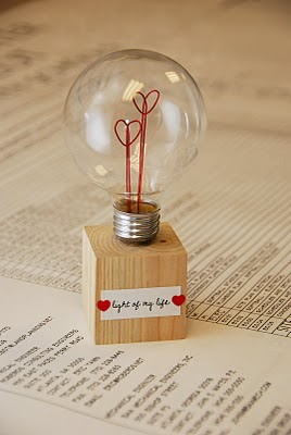 round light bulb with 2 wire red hearts on a wood block that has a paper saying light of my life