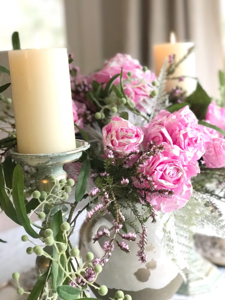 pink tissue paper bouquet with much greenery and 2 white candle on blue and gold distressed candle holders