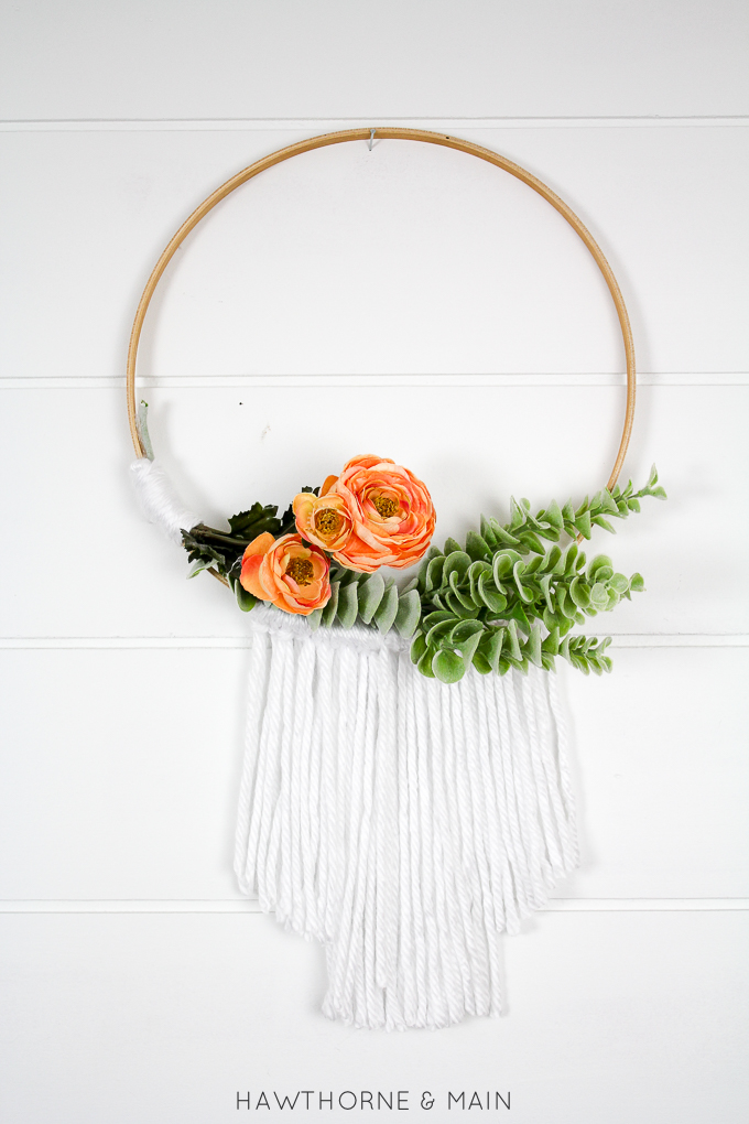 embroidery hoop wall hanging with white yarn on the bottom. orange flowers and greenery