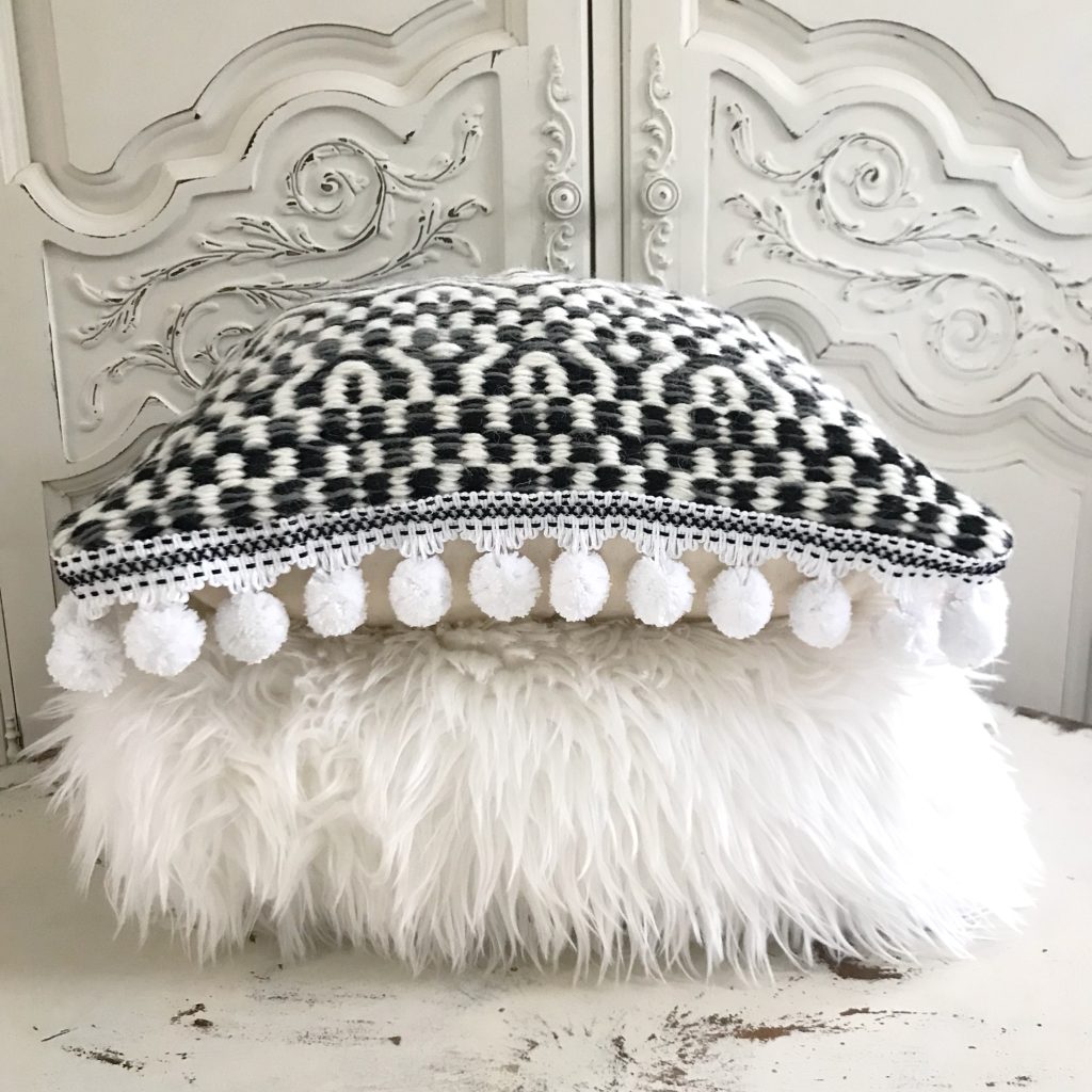 fur white pillow laid flat with black and white pillow with pom poms on edge laid on top