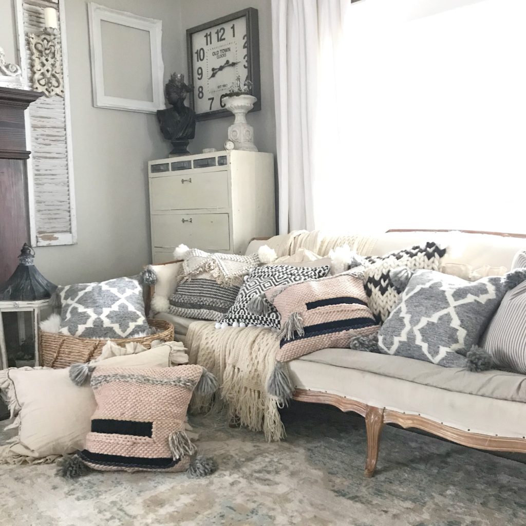 white couch with 7 pillows on it and 2 farmhouse pillows on the ground and then one in a basket next to the couch