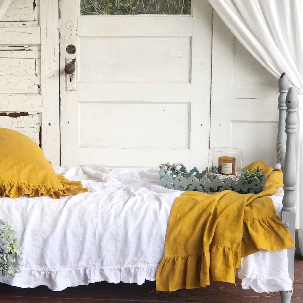 white ruffle bed with yellow pillows and linen bed blanket with blue tray sitting on bed 