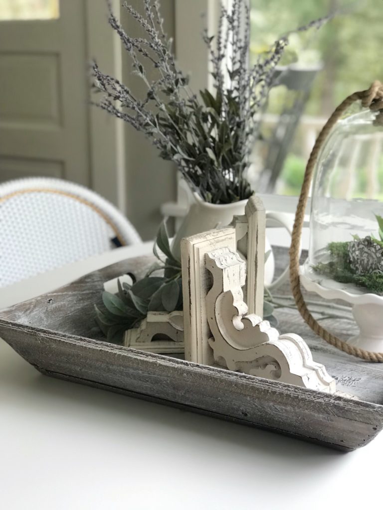 white table with wood tray filled with white corbel and white vase of lavender and cloche with rope