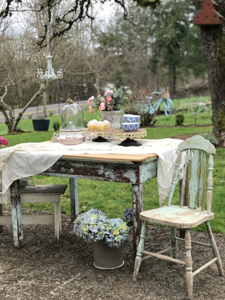 blue farmhouse table and chair with white table cloth and 2 cake stands