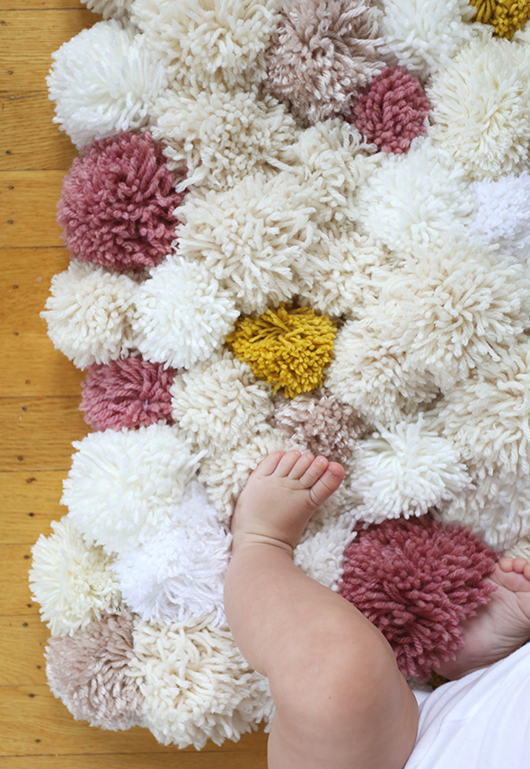 white and pink and yellow pom pom rug with baby legs on it