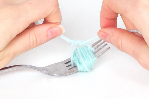 blue yarn wrapped around a fork and lady tying it