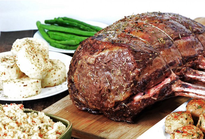 prime rib on cutting board with food surrounding it
