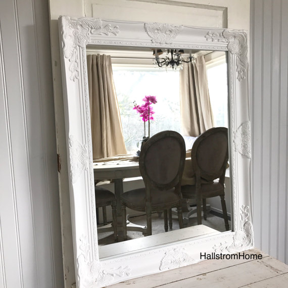 white mirror sitting on cream table in reflection is chairs and table with pink flower