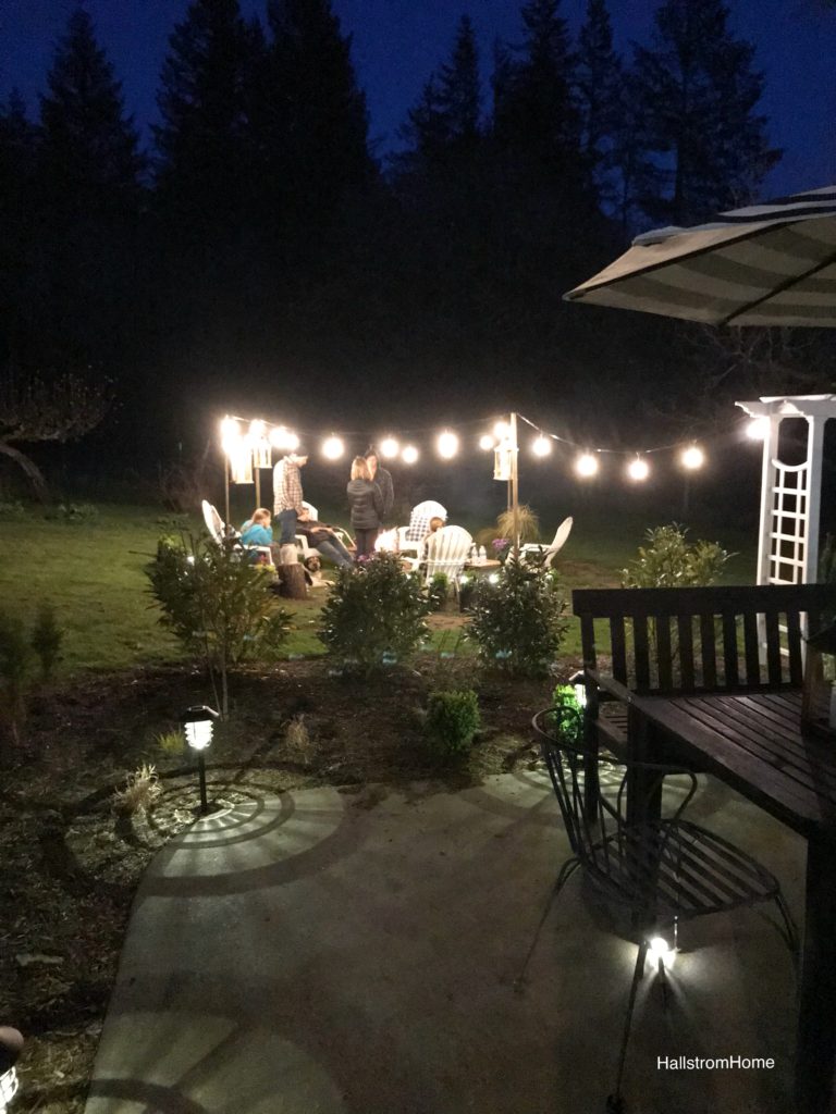 The Girl Who Built a Beautiful Fire Pit white lawn chairs around heelbarrow lit fire. lights draped around border seating area