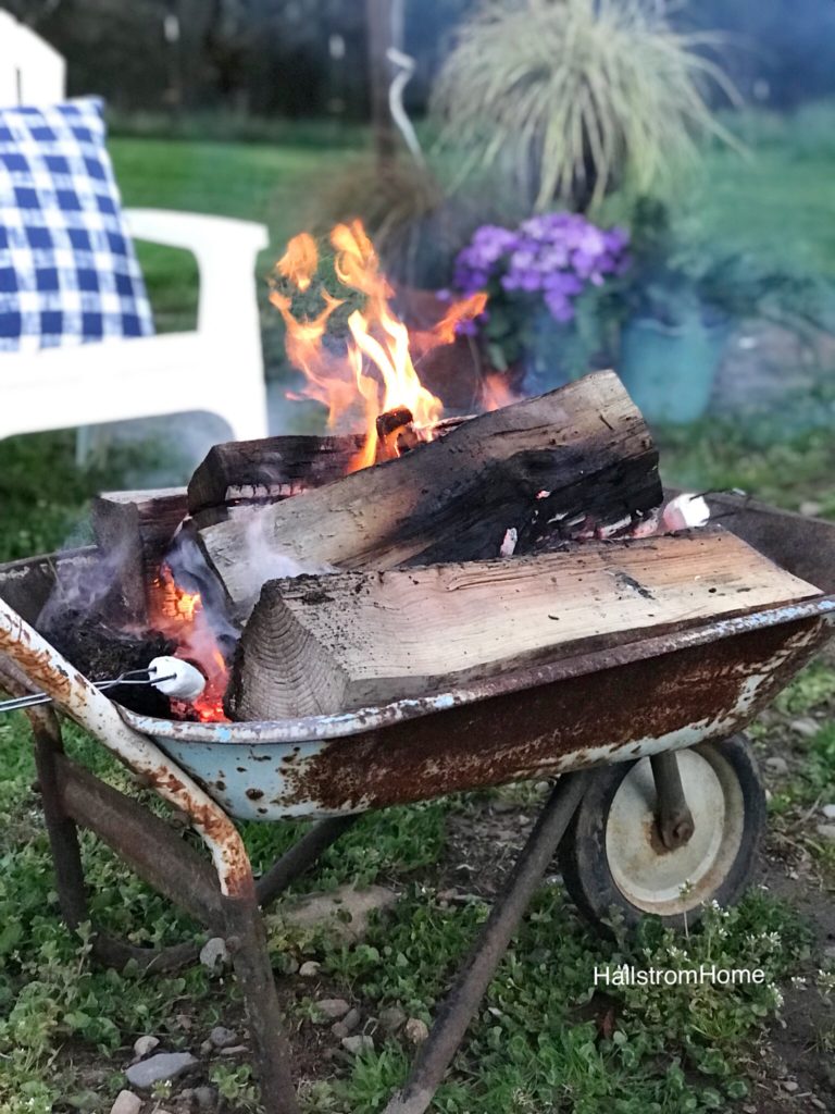 rusty blue wheel barrow fire place white white chair in background and purple flowers