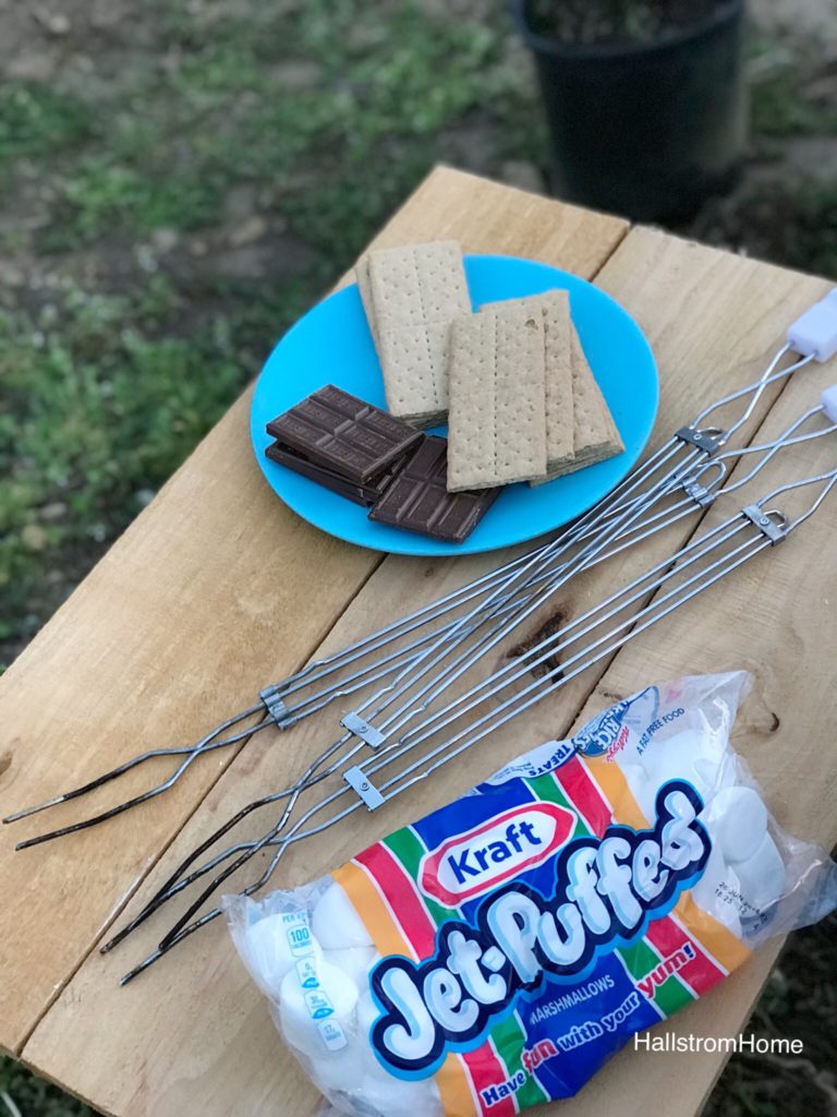 blue place with stack of chocolate and graham crackers with roasting sticks and marshmallow bag on wood table