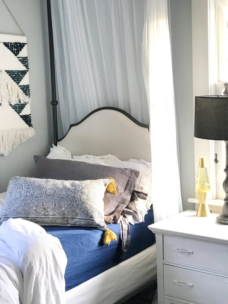 twin bed with blue sheets and a white pillow and gray linen pillow and blue patterned pillow