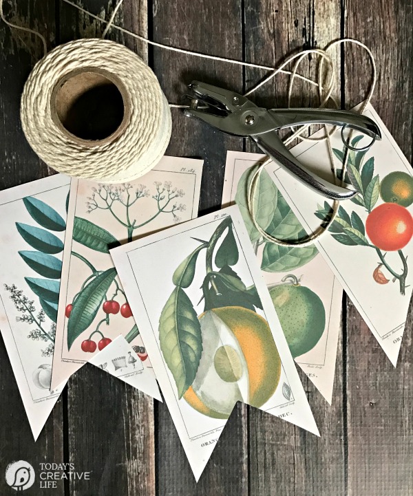 5 banner pieces with botanical prints on them and a spool of twime and hole puncher laying on wood table