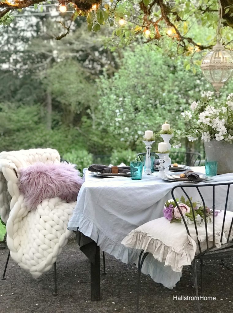 ruffle linen table cloth with 2 black charis and 3 white candle sticks and silver bucket with white flowers in it