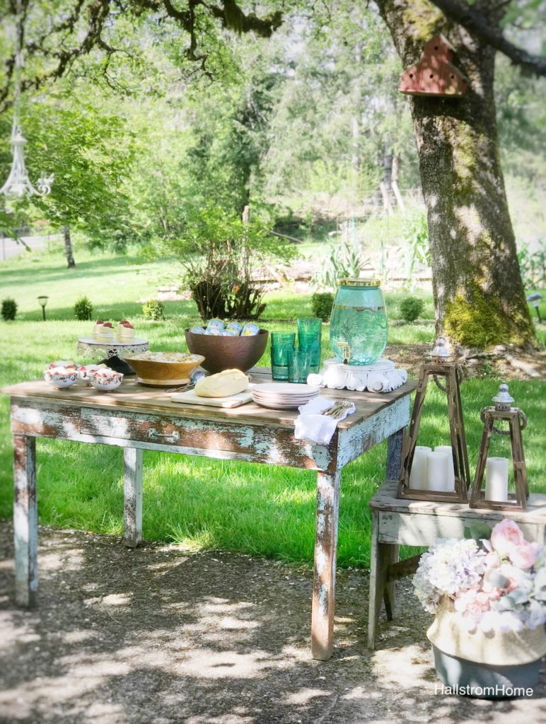 woodend table with blue pitcher stack of pink plates white linen napkins with gold silverware