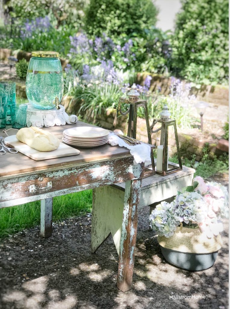 woodend table with blue pitcher stack of pink plates white linen napkins with gold silverware