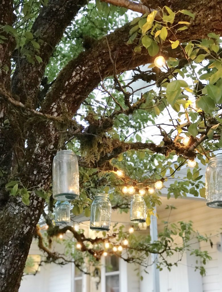 3 blue mason jars hanging from tree with lights