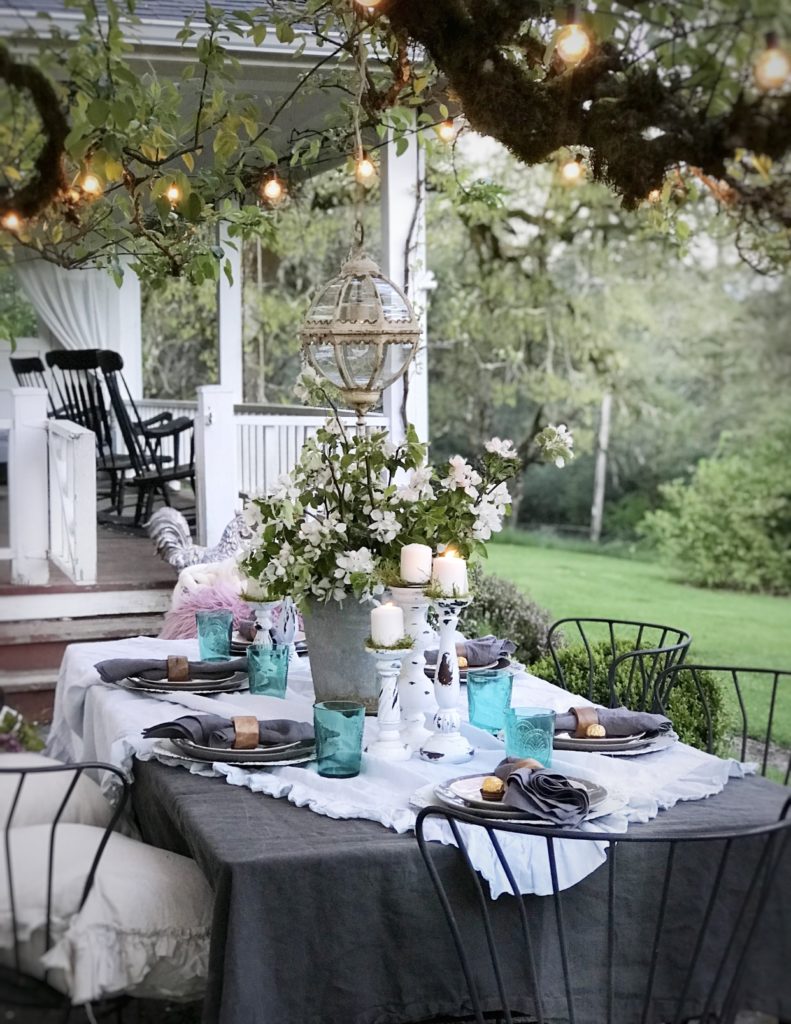 ruffle linen table cloth with 6 white candle holders and blue cups silver bucket with white flowers and round glass chandeleier