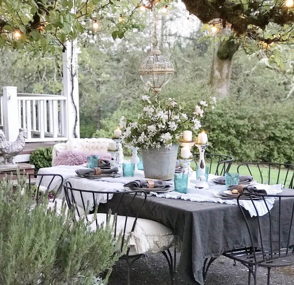 ruffle linen table cloth with 6 white candle holders and blue cups silver bucket with white flowers and round glass chandeleier