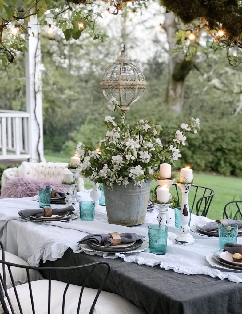 ruffle linen table cloth with 6 white candle holders and blue cups silver bucket with white flowers and round glass chandeleier