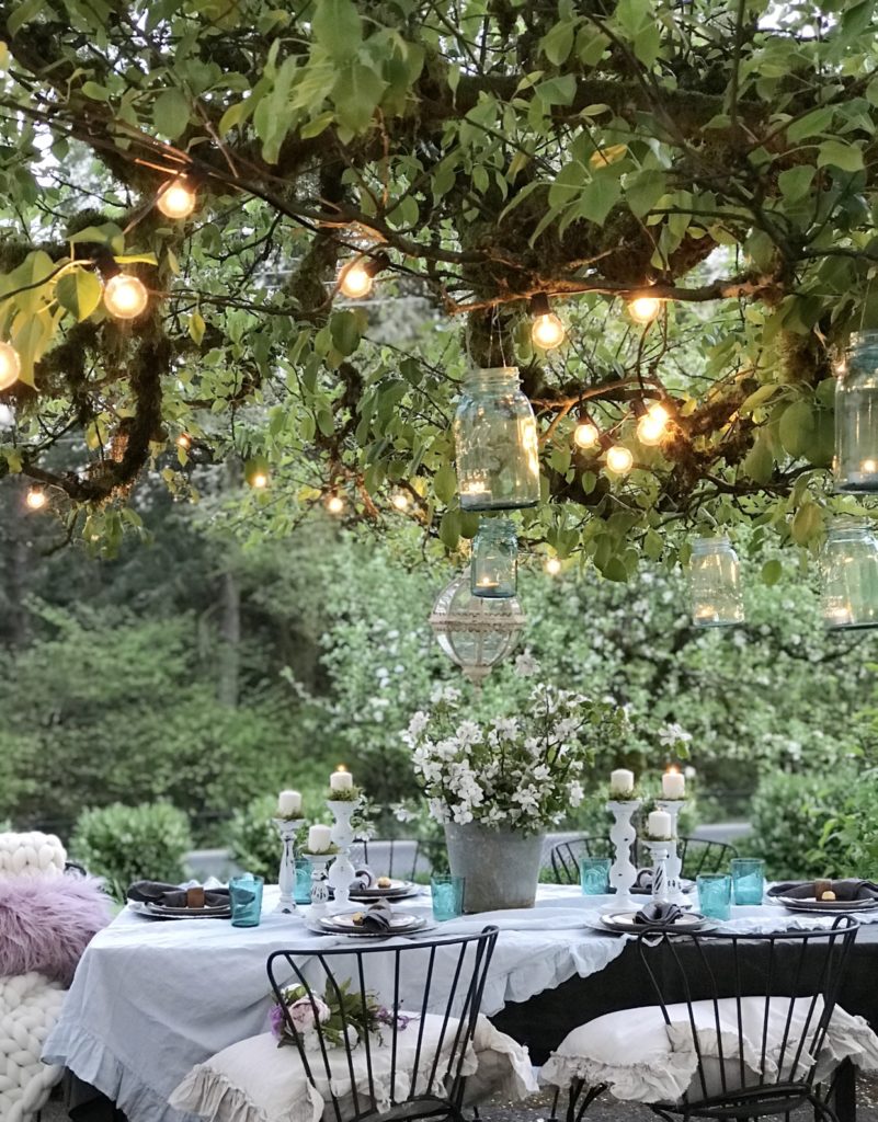 ruffle linen table cloth with 6 white candle holders and blue cups silver bucket with white flowers and round glass chandeleier